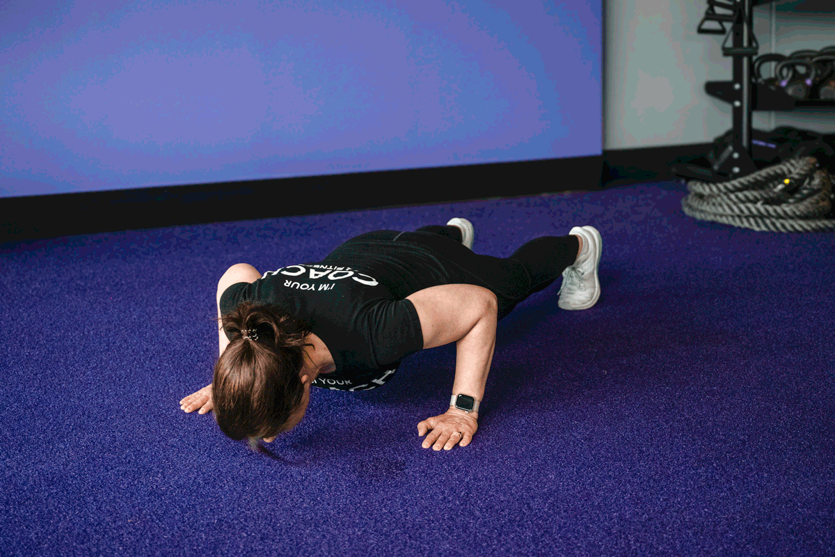 Personal trainer performing push-ups, focusing on chest, shoulders, and triceps. The image captures the trainer in the down position.