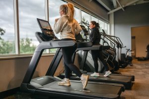 Two women running on treadmills at an Anytime Fitness gym, focusing on fitness and cardio exercise with a scenic window view.