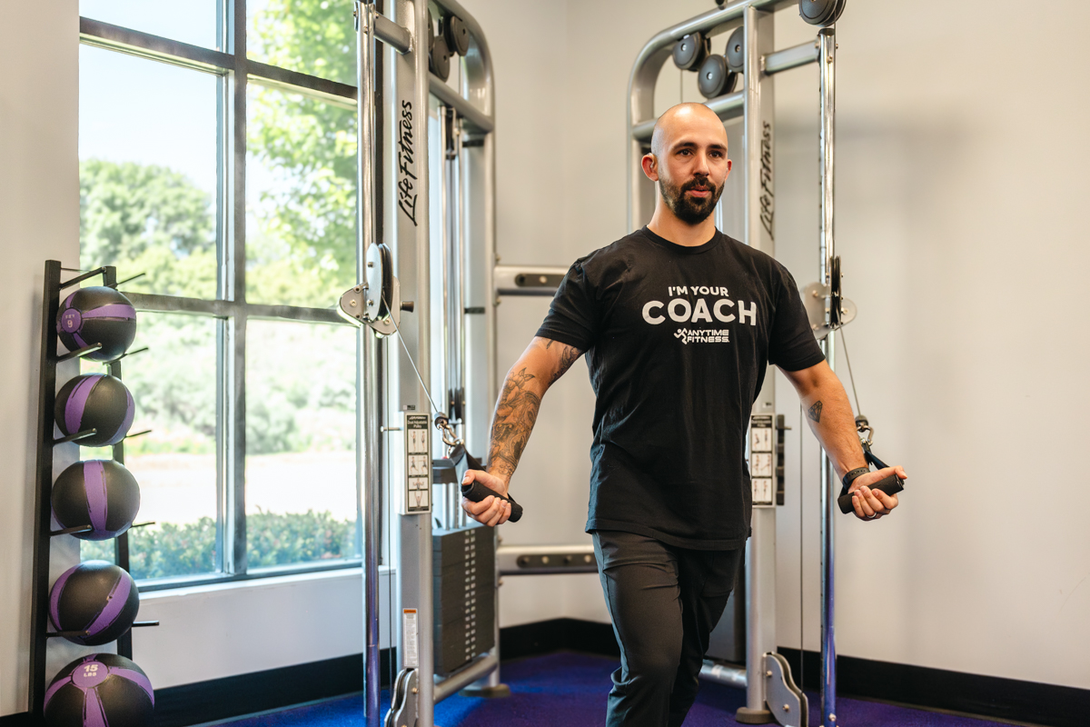 Personal trainer completing the high pulley crossover exercise, with cables crossed and lower chest muscles fully contracted. The image illustrates the final position, demonstrating proper form and technique.