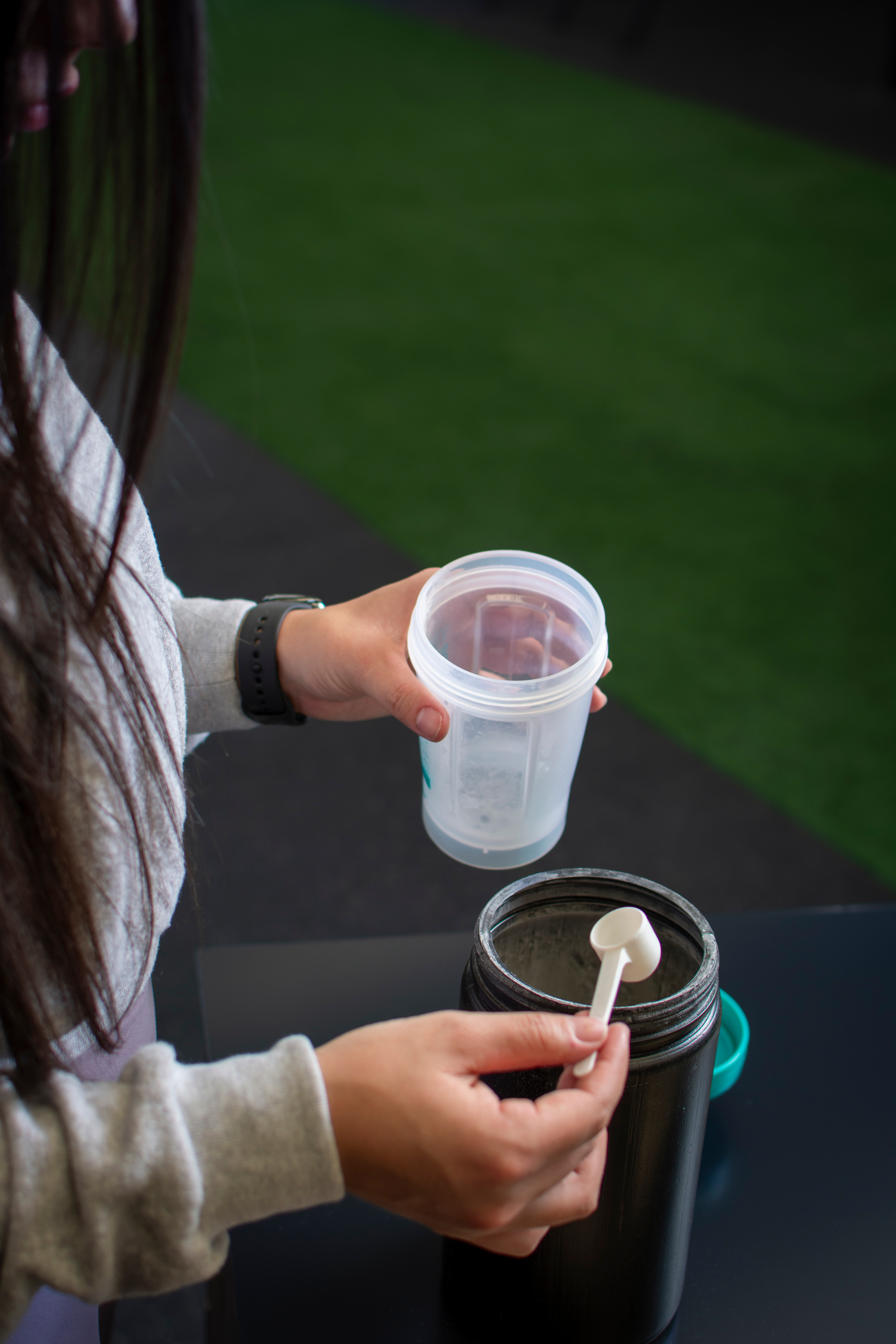 Athlete scooping a supplement into a shaker bottle after a workout.
