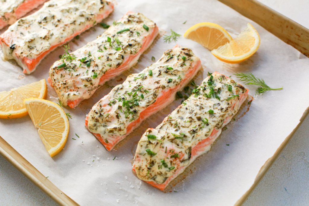 Baked herb-crusted salmon filets on a parchment-lined baking sheet, garnished with fresh herbs and served with lemon wedges.