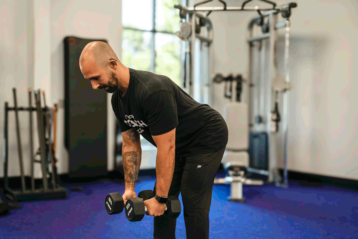 Anytime Fitness coach demonstrating bent over lateral raise exercise with dumbbells, targeting shoulder and upper back muscles.
