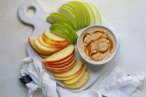 Thinly-sliced red and green apples next to a small ramekin of peanut butter caramel apple protein dip.