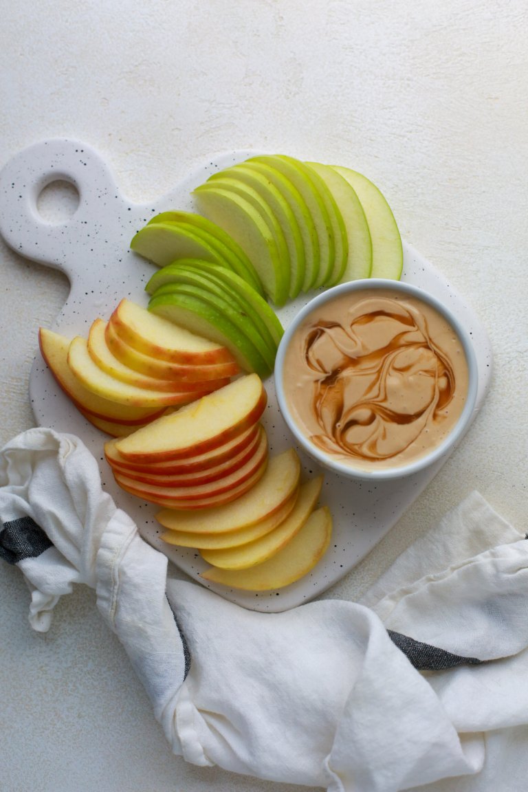 Thinly-sliced red and green apples next to a small ramekin of peanut butter caramel apple protein dip.