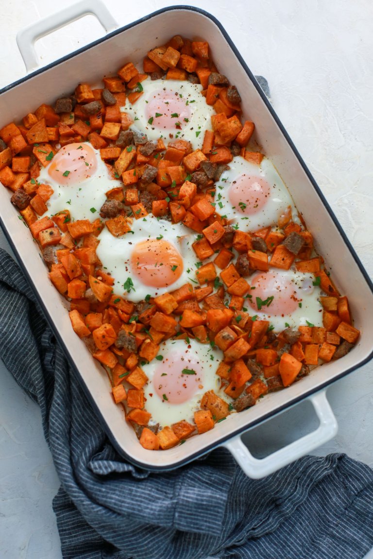 Breakfast casserole made with cubed sweet potatoes, eggs and seasoning in a ceramic baking pan with a napkin nearby.