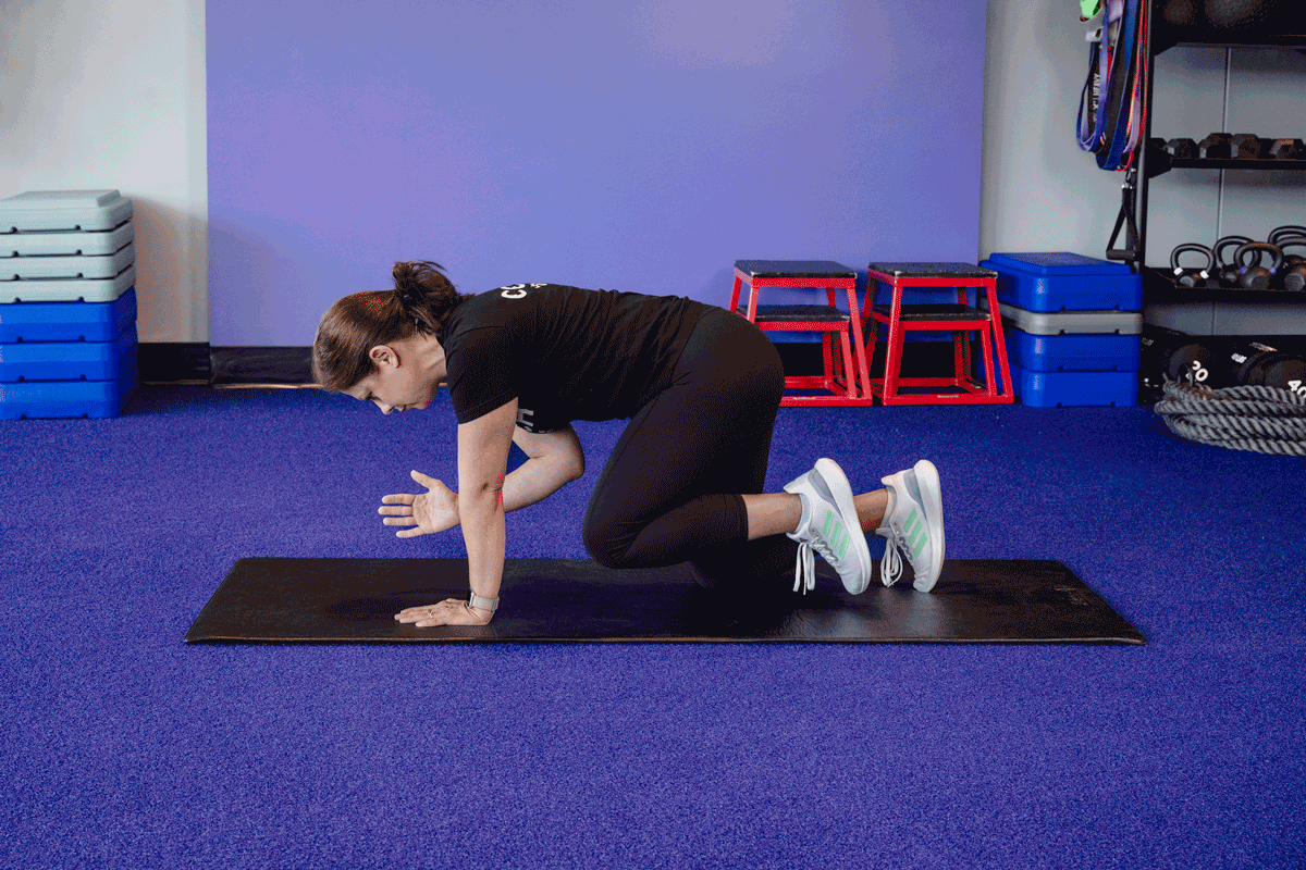 A woman executes a bird dog exercise on a mat. Positioned on all fours, she extends her right arm and left leg simultaneously, engaging her core for balance and stability.