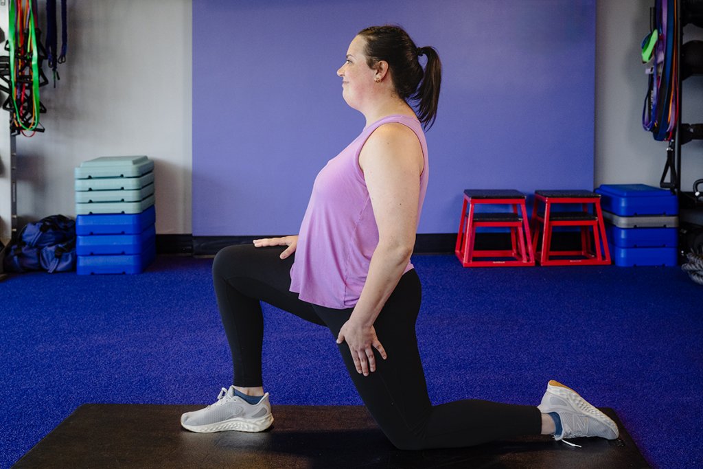 Woman in a half kneel position while doing a workout in a gym environment.