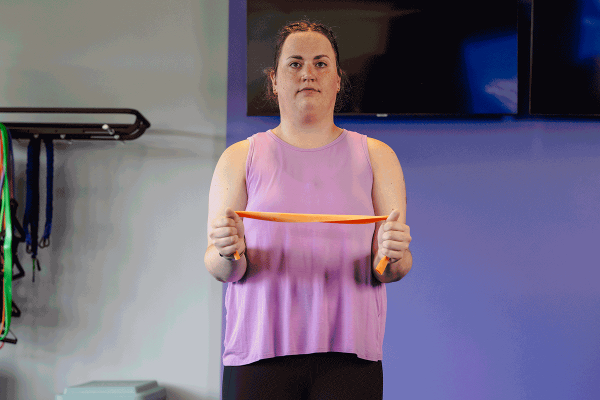 Woman executing a shoulder W exercise using a resistance band to strengthen upper back muscles and enhance posture in a gym.