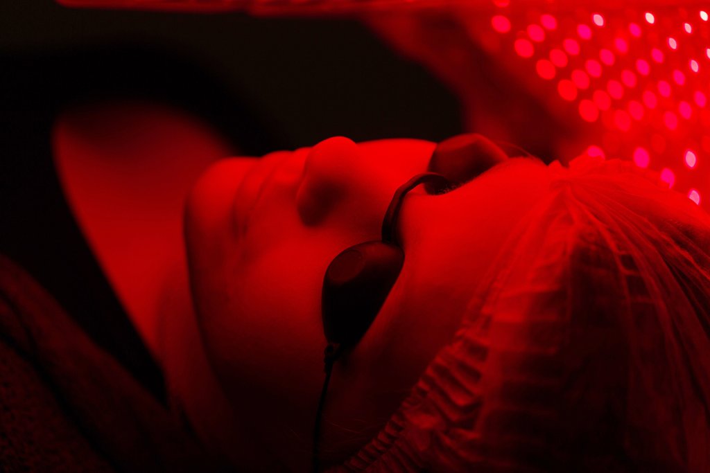 Person lying in a red light therapy bed wearing eye protectors.