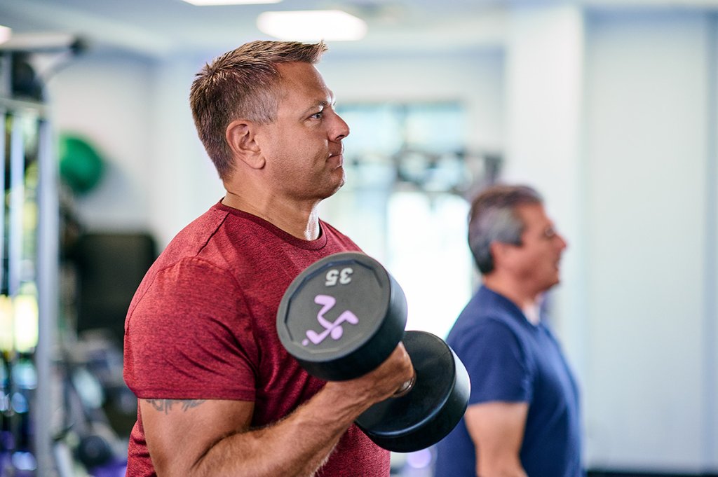 Middle-aged man in a red shirt performing bicep curls with a 35-pound dumbbell at the gym, focusing on strength training and muscle building.