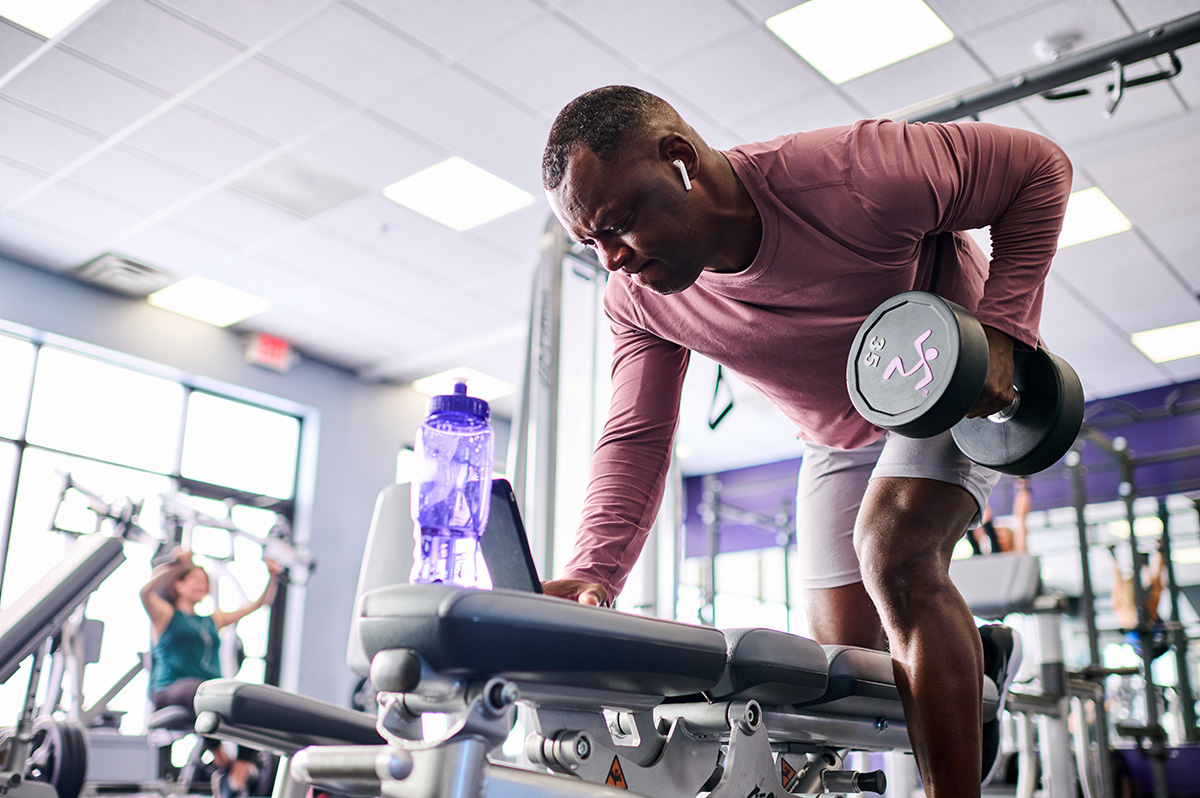 Man in a maroon long-sleeve shirt doing a one-arm dumbbell row at the gym, emphasizing back strength and muscle conditioning.