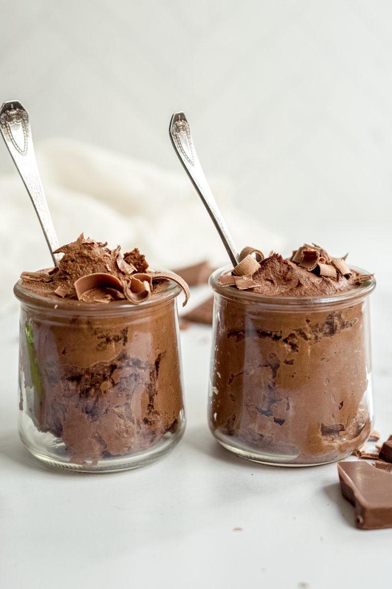 Two jars of chocolate pudding topped with shaved chocolate, with serving spoons.