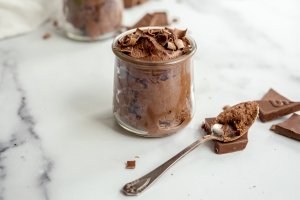 Jar of chocolate pudding topped with shaved chocolate, with a serving spoon.