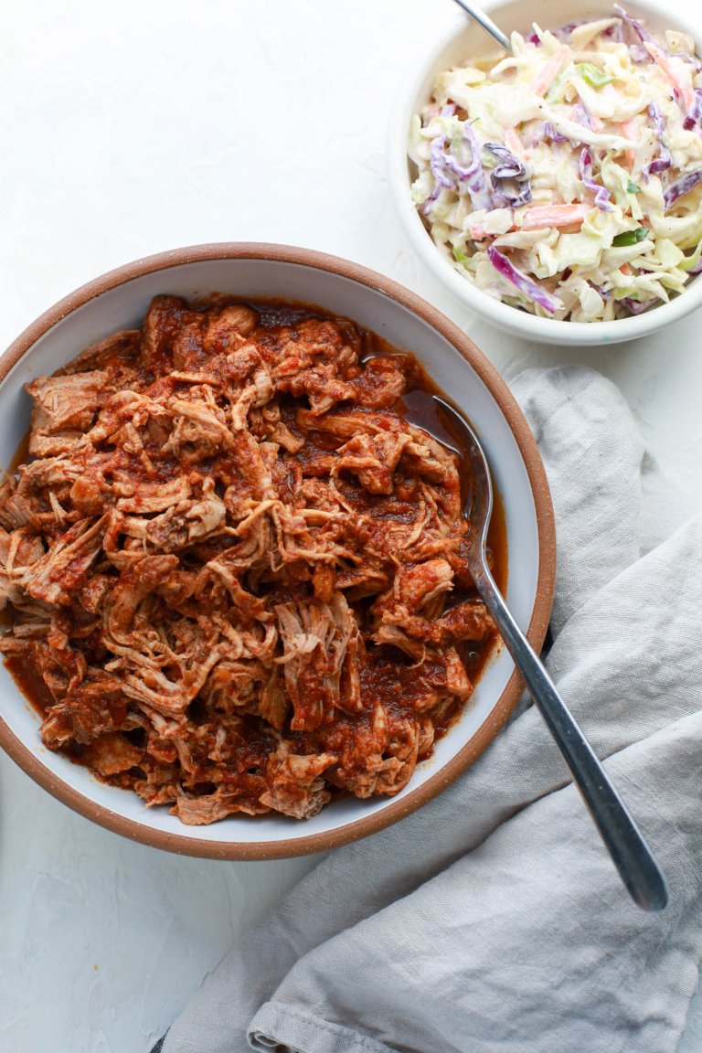 Bowl of shredded raspberry chipotle pork tenderloin, ready to serve with a spoon, next to a bowl of coleslaw.