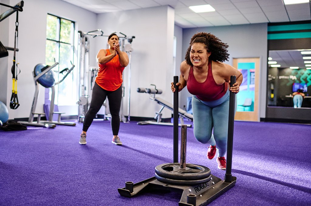 Woman pushing a weighted sled in a gym during a high-intensity workout for weight loss.