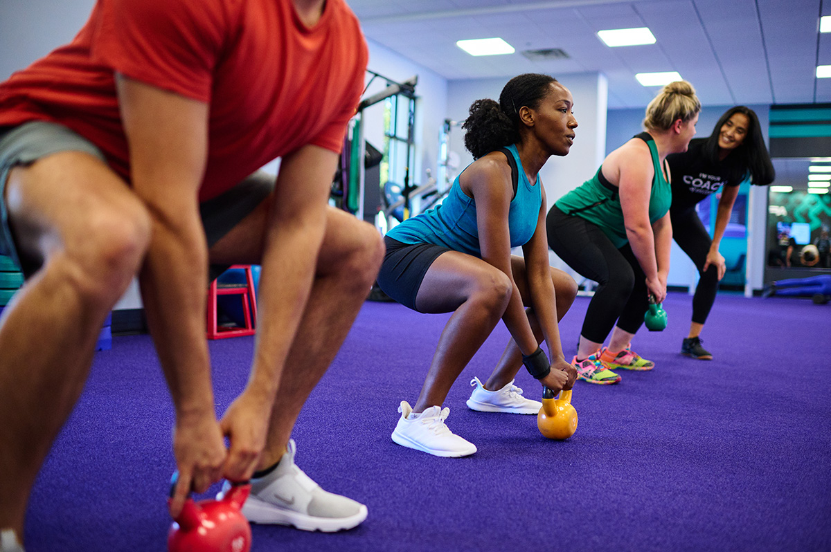 Group of individuals performing kettlebell squats in a gym, during a full-body workout for burning calories and building muscle.