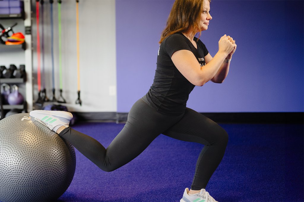 Woman performing a Bulgarian split squat using a stability ball in a gym setting.