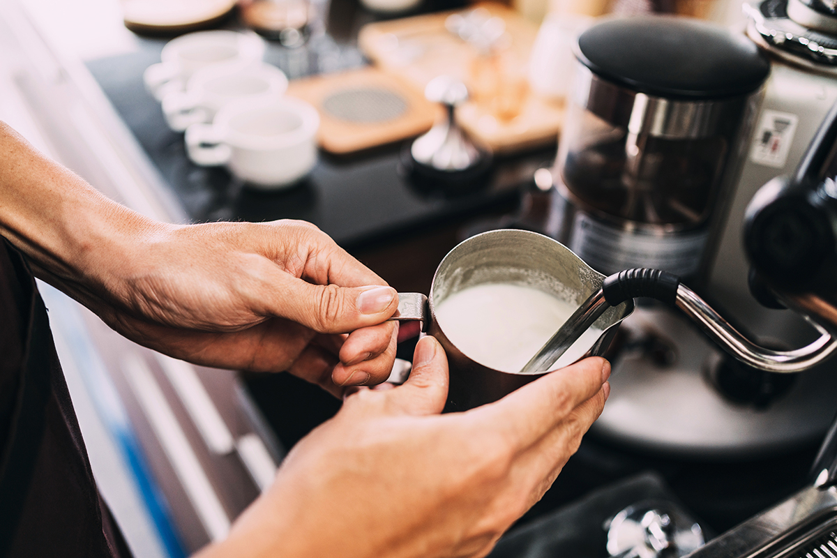 Barista using an espresso machine to froth milk.