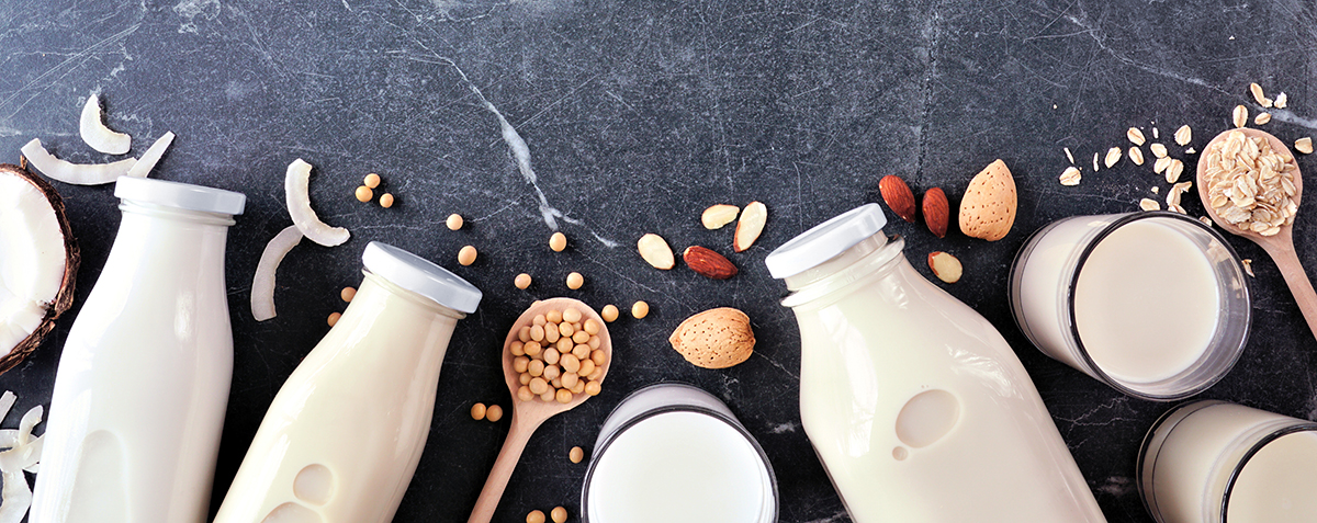 Overhead shot of bottles and glasses of milk next to oats, almonds, and other nuts.