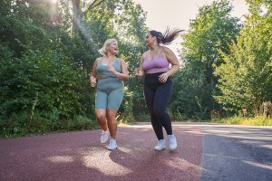 Positive woman looking at her running partner and laughing while jogging on the street together.