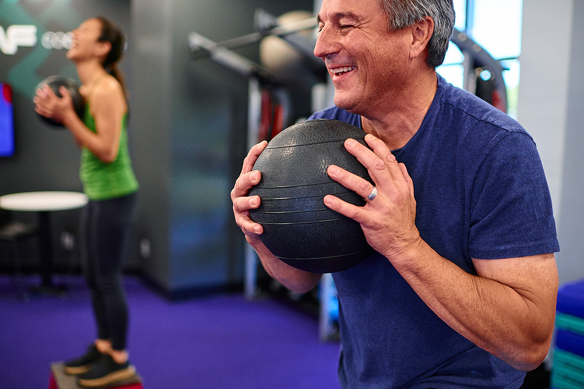 Man holding an exercise ball in a gym setting.