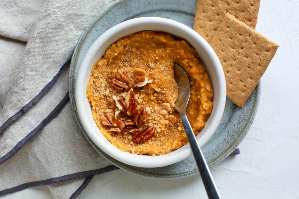 Bowl of pumpkin pie-flavored oats with chopped pecan topping and a side of graham crackers.