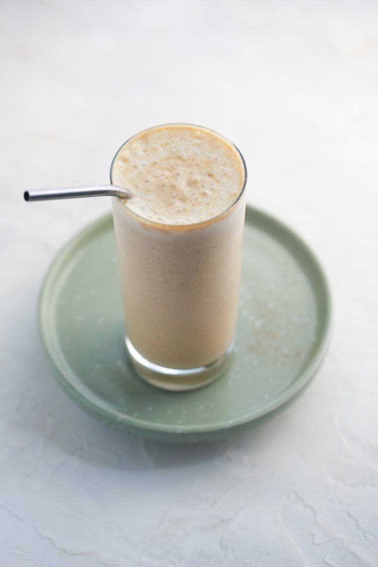 Blended protein shake in a glass with a creamy layer of foam on top and a straw ready for drinking.