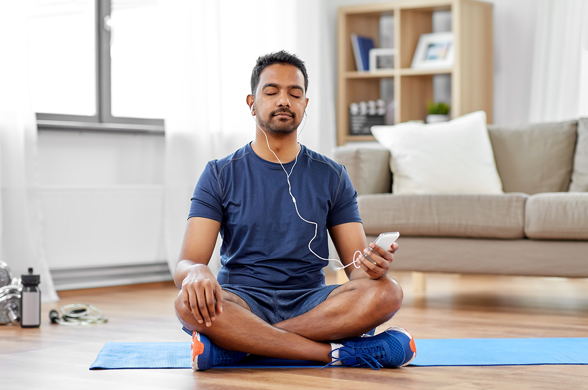 Man meditating in a seated position at home, listening to calming music, focusing on mental wellness and relaxation.