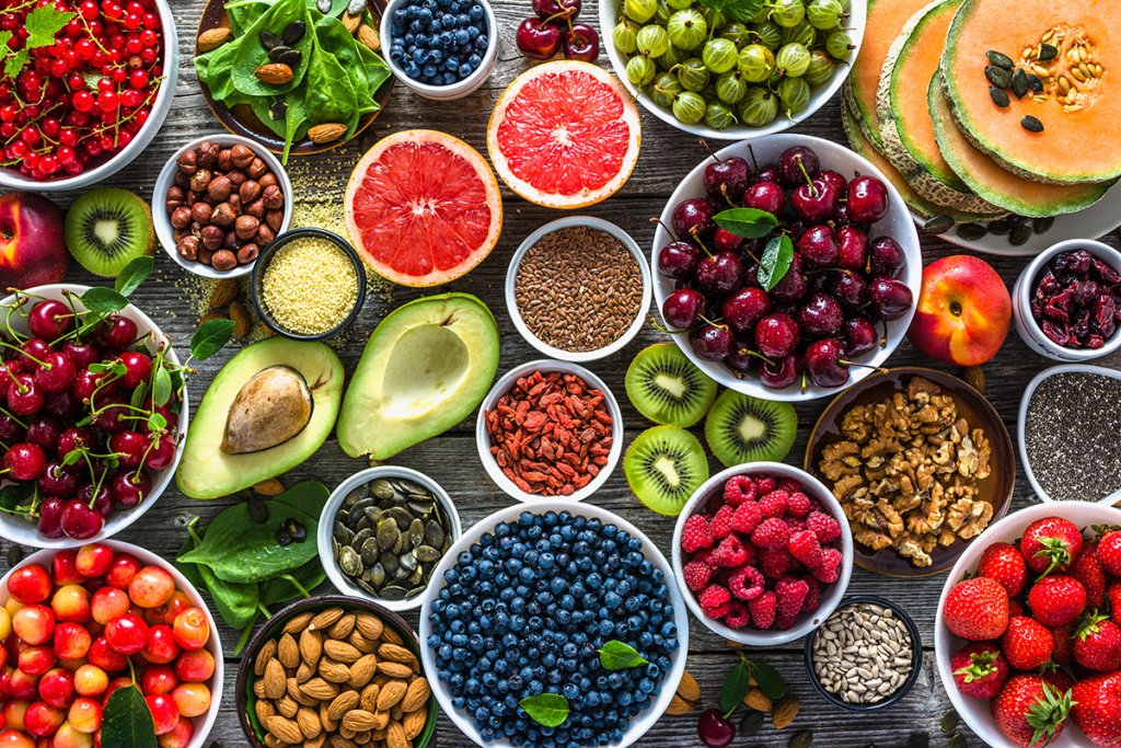 A colorful spread of fruits, seeds, and nuts on a wooden surface, showcasing nutrient-dense foods like berries, avocado, almonds, and grapefruit.