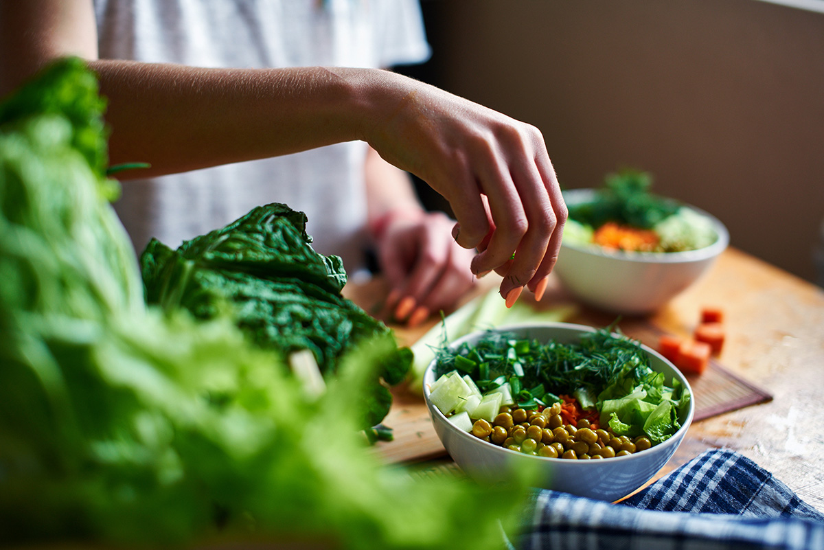 A person preparing a healthy salad with leafy greens and vegetables, sprinkling herbs on top.