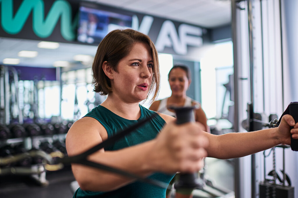 Woman focused and determined while using resistance bands in a gym workout at Anytime Fitness.