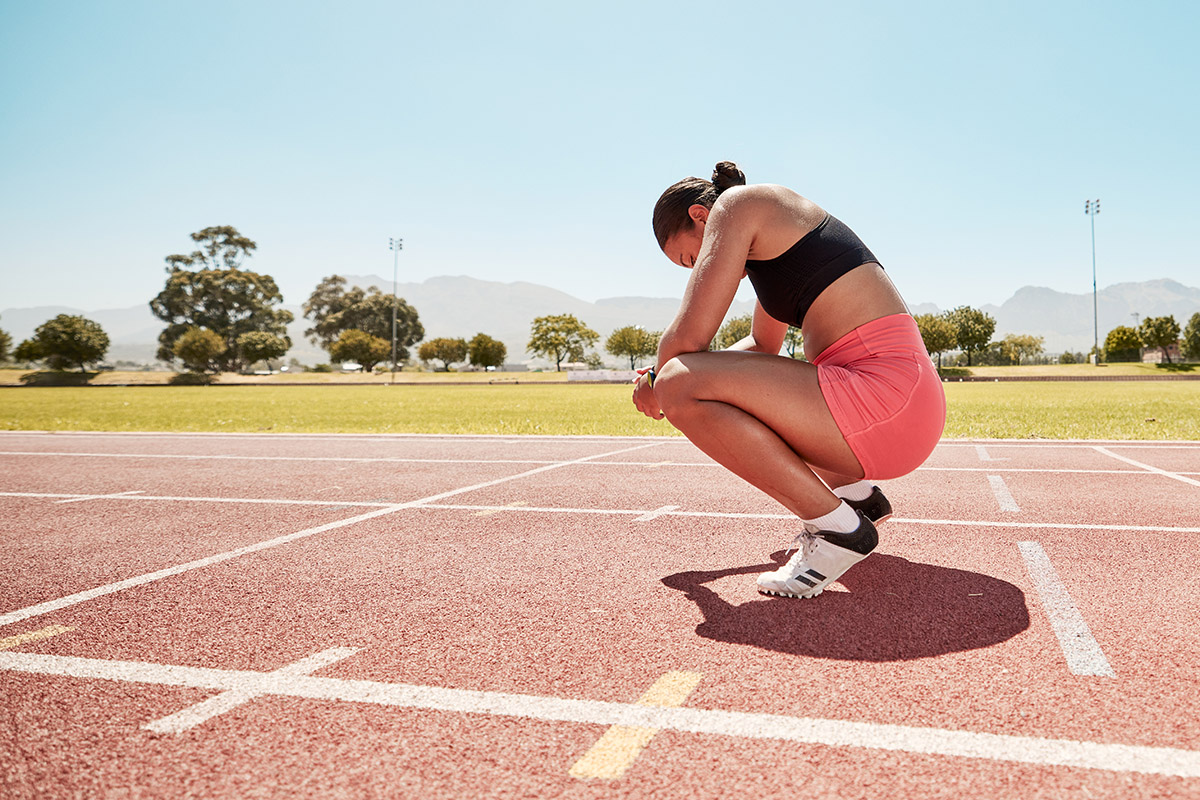 Female athlete crouching on a track, taking a break during an outdoor training session on a sunny day.