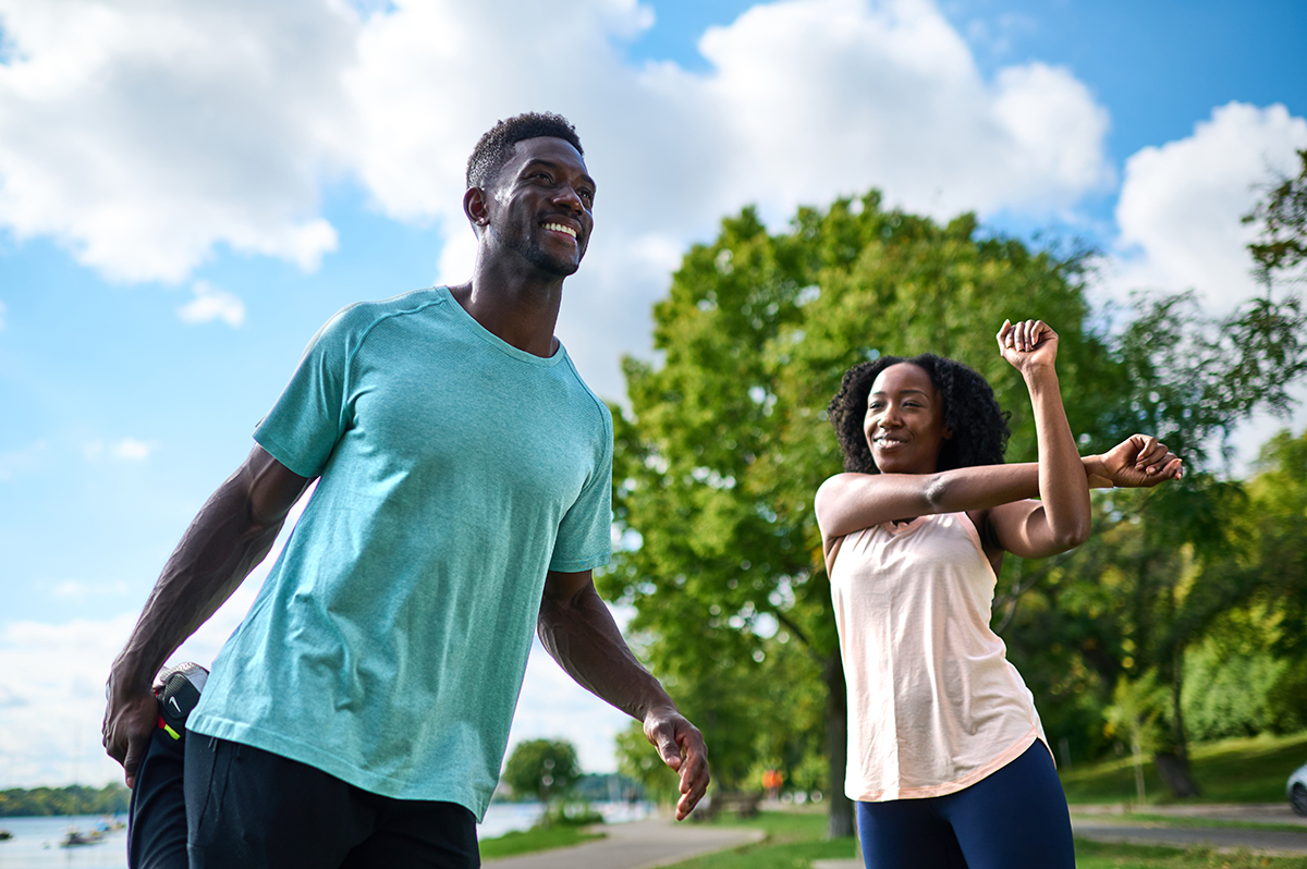 Fit couple stretching and warming up together outdoors by the lake, enjoying a sunny day and green scenery.