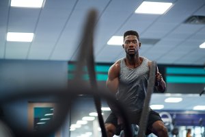 Focused man performing a battle rope exercise in a gym. Strength and endurance training showcasing high-intensity workout for building upper body strength and cardiovascular fitness.