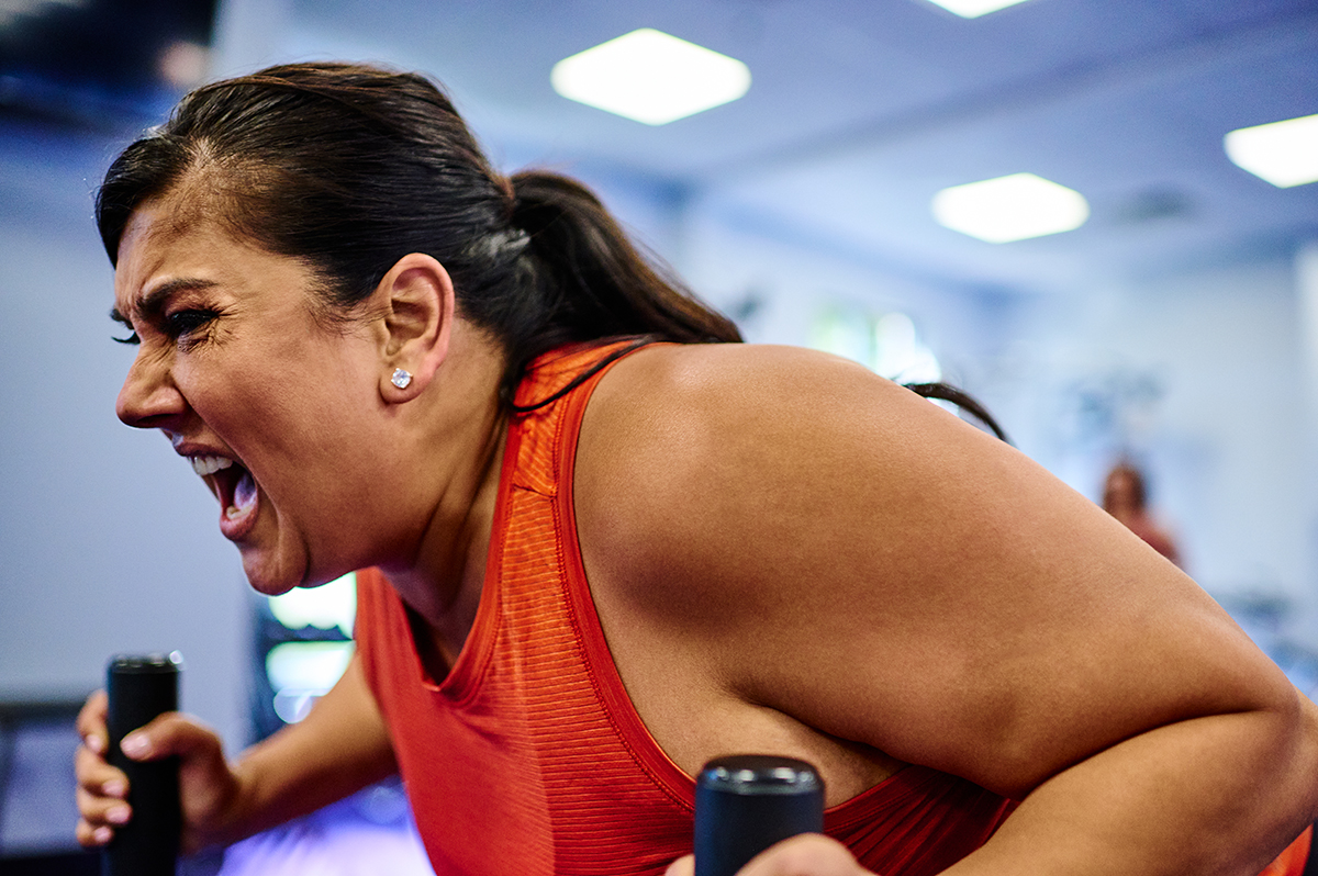 Woman pushing through an intense workout on gym equipment, displaying focus and effort during a high-intensity training session. Fitness motivation, strength training, and perseverance during exercise.