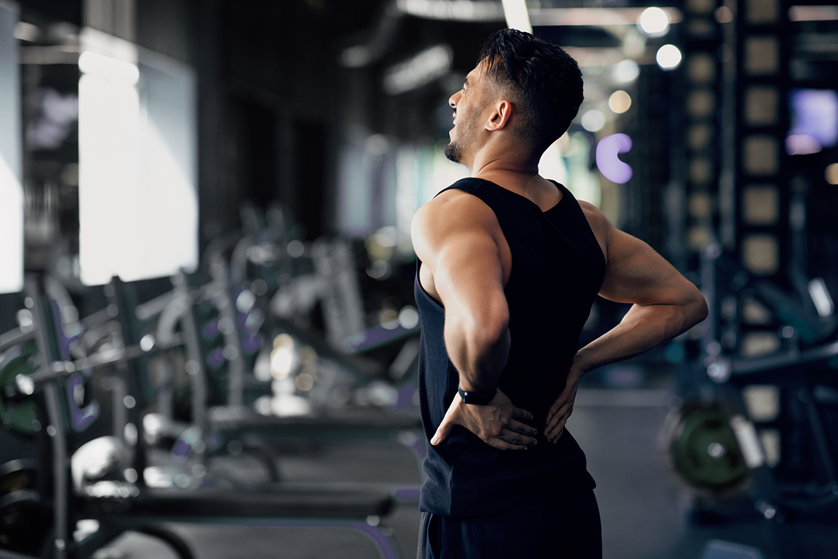 Athletic man in a gym holding his lower back, indicating back pain or muscle strain.