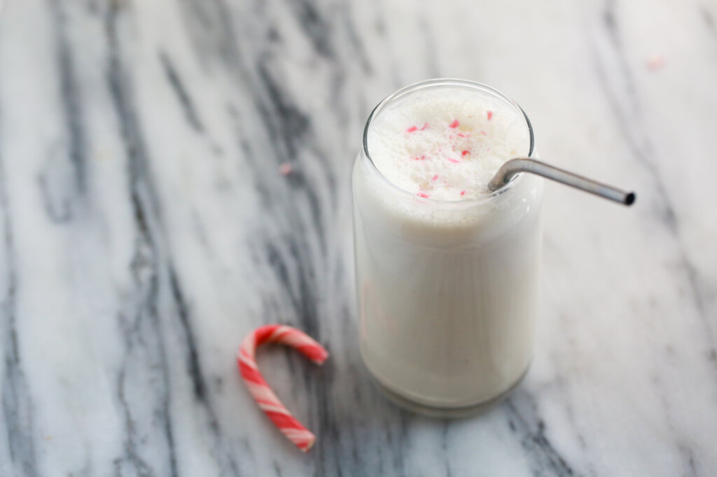 Peppermint protein shake in a glass with a straw ready to drink. Candy cane garnish on top of foamy shake.