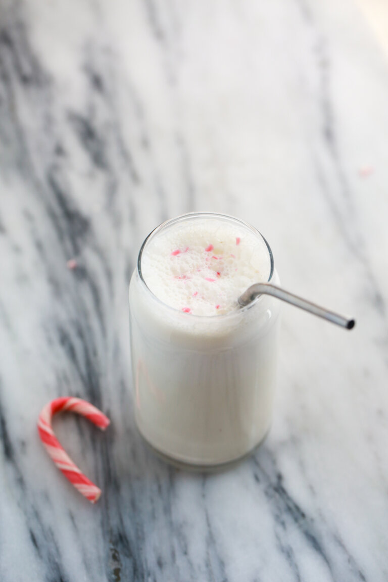 Peppermint protein shake in a glass with a straw ready to drink. Candy cane garnish on top of foamy shake.