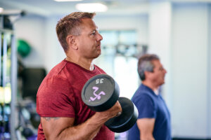 A man in a red shirt lifting a 35-pound dumbbell at the gym, showcasing focus and determination during his strength training workout.