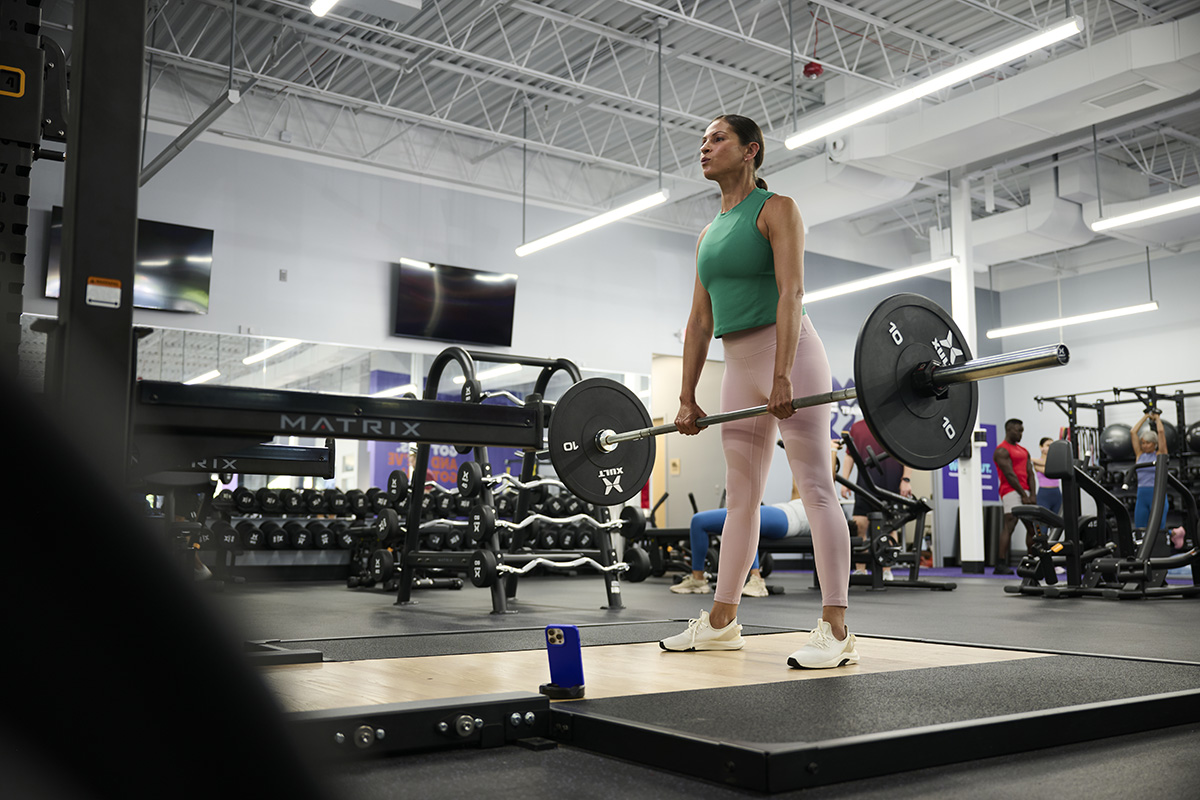 A woman performing a barbell deadlift in a well-equipped gym, showcasing strength and proper weightlifting form.